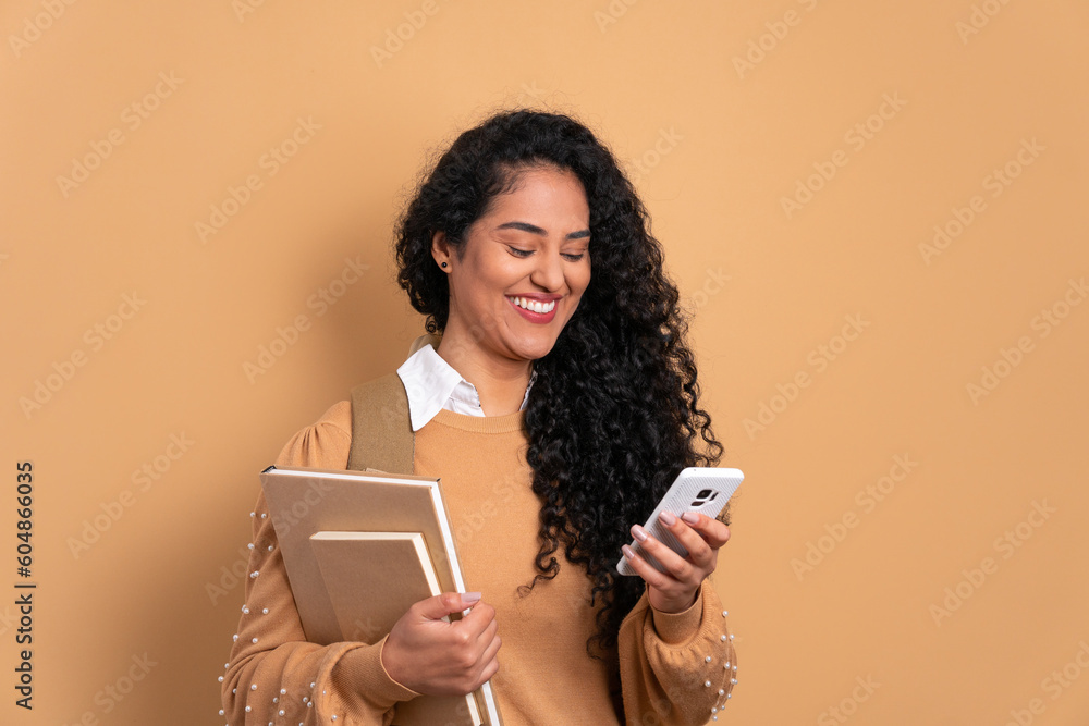 joyful black young woman looking at mobile cell phone screen in beige background. dedication, effort education concept. joyful black young woman looking at mobile cell phone screen in beige background. dedication, effort education concept.