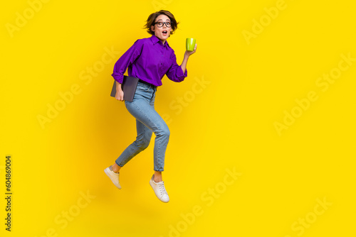 Full length photo of impressed woman dressed purple shirt jumping holding gadget drink tea empty space isolated yellow color background