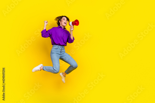 Full length photo of cool lucky lady wear violet shirt jumping shouting bullhorn empty space isolated yellow color background