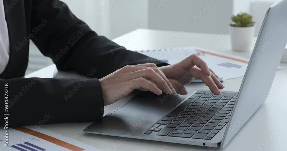 A close-up shot of the hands of a young Indian woman typing actively on a laptop placed on a desk with scattered papers. Her focused and skillful typing reflects productivity and determination.