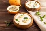 Yoghurt with granadilla and mint in wooden bowl on brown wooden, side view.