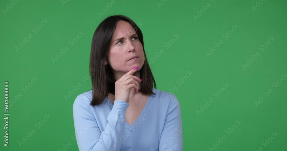 A Caucasian woman stands on a green background, deep in thought. She looks around, puts her hand under her chin. Suddenly, she gets a perfect idea and shows a thumbs-up gesture to express excitement. A Caucasian woman stands on a green background, deep in thought. She looks around, puts her hand under her chin. Suddenly, she gets a perfect idea and shows a thumbs-up gesture to express excitement.