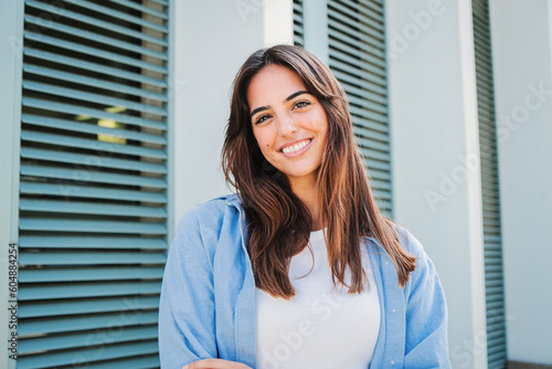 Happy caucasian young student female looking at camera enjoying with a perfect white teeth. Portrait of a joyful and adorable teenage brunette woman posing for a college promotion with crossed arms
