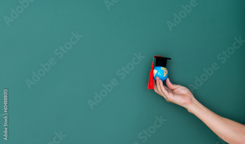 Billede på lærred Hand hold a globe and mortarboard in front of blackboard