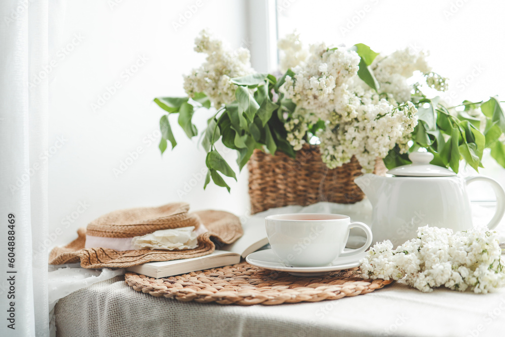 Cup of tea and teapot on windowsill and basket with white lilacs, good morning concept Cup of tea and teapot on windowsill and basket with white lilacs, good morning concept