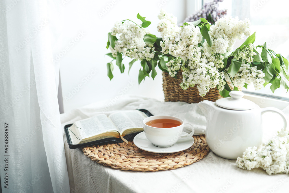 A cup of tea, a basket of lilacs and an open Bible A cup of tea, a basket of lilacs and an open Bible