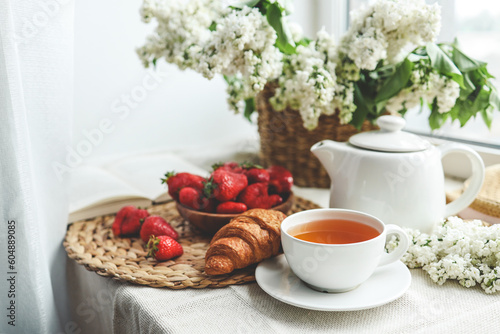 Cup of tea, croissant, strawberry and lilac basket, summer morning aesthetic