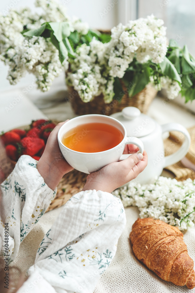 Cup of tea in hands, strawberries and flowers, summer breakfast concept