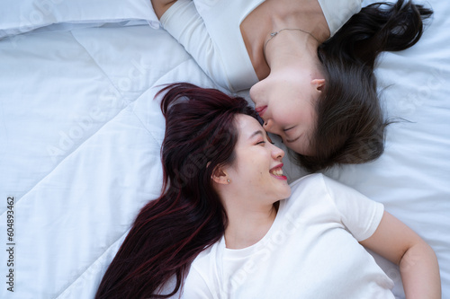 On a white bed, an LGBT couple is gently kissing each other's foreheads.