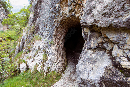 Rock wall with a dark hole, entrance to the cave in Jura mountains, hiking trail, Gorges de Court, Switzerland