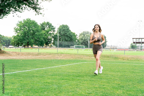 Young blond slim fit sporty woman with well-groomed long hair in stylish fitness clothes and sneakers jogging outside on football grass lawn field on summer day. Fitness, jogging, footwear, lifestyle