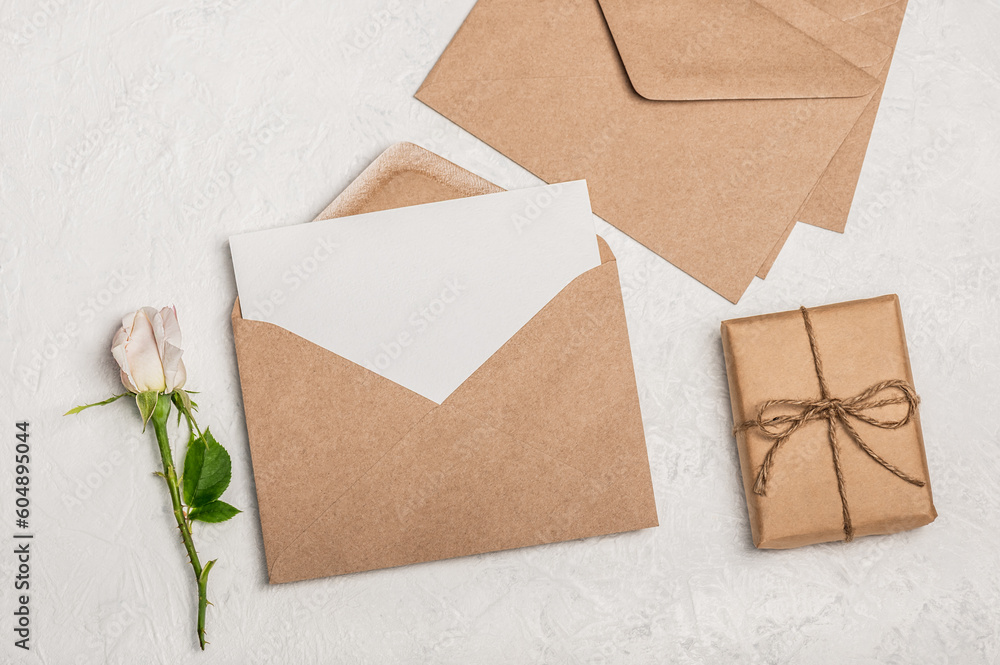 Feminine Invitation or greeting card mockup with craft envelope, gift box and white rose on light background. Feminine Invitation or greeting card mockup with craft envelope, gift box and white rose on light background.