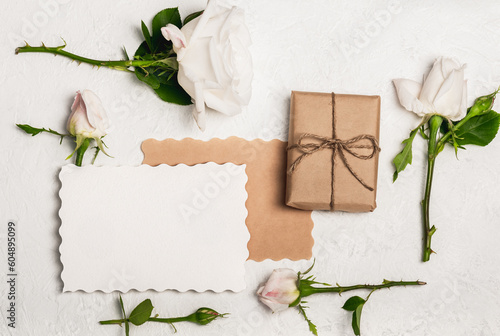 Feminine Invitation or greeting card mockup with gift craft box and white roses on light background.