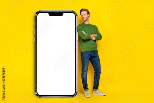 Full length photo of cute dreamy man wear pullover arms crossed looking gadget empty space isolated yellow color background