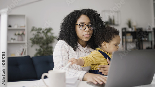 Mother is holding her child on knees and talking at an online conference, unpaid parental leave
