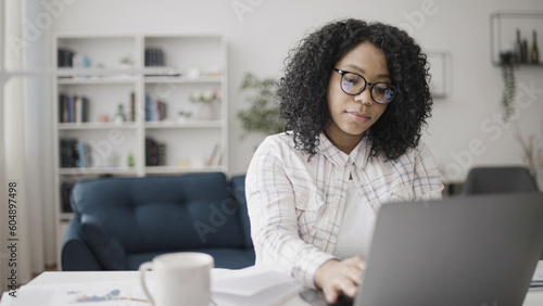 An attractive African American woman in eyeglasses working on her laptop in home office