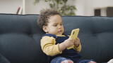 Cute African American toddler holding smartphone, looking at screen, smiling