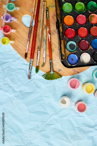 Flat lay of colorful paints, painting palette and brushes on blue background, art, painting and hobby concept, top view, copy space..