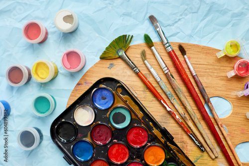 Flat lay of colorful paints, painting palette and brushes on blue background, art, painting and hobby concept, top view, copy space..
