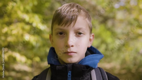 A cute young boy looks seriously at the camera in a forest - closeup
