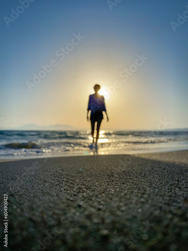 Low angle view of blurred woman walking in backlit on a beach at sunset.