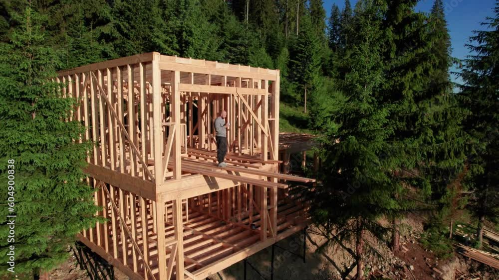 Client is having wooden frame house built near the forest, drinking a cup of coffee. The concept behind it is modern and environmentally friendly construction. Client is having wooden frame house built near the forest, drinking a cup of coffee. The concept behind it is modern and environmentally friendly construction.