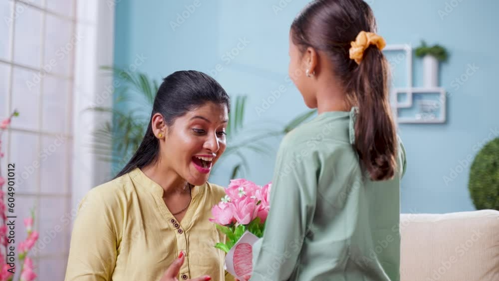 Shoulder shot of indian girl kid giving flowers with greeting card to mother by hugging at home - concept of mother's day, togetherness and motherhood. Shoulder shot of indian girl kid giving flowers with greeting card to mother by hugging at home - concept of mother's day, togetherness and motherhood.