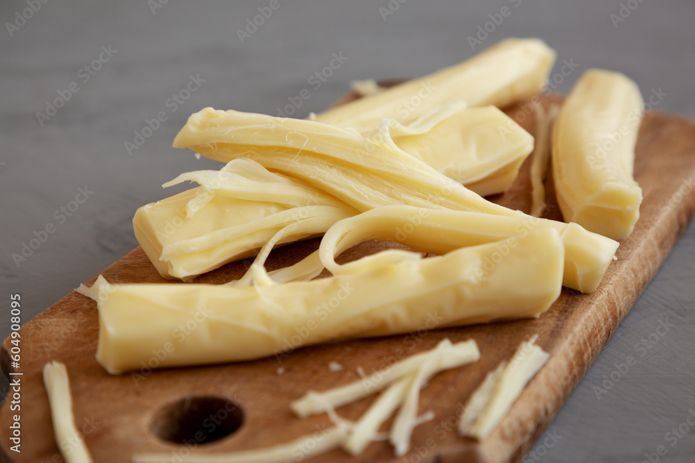 Organic String Cheese on a rustic wooden board on a gray background, side view. Close-up. Organic String Cheese on a rustic wooden board on a gray background, side view. Close-up.