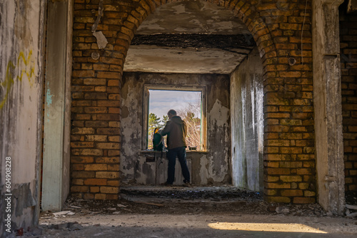 A man in a green jacket looks out the window of an abandoned building.