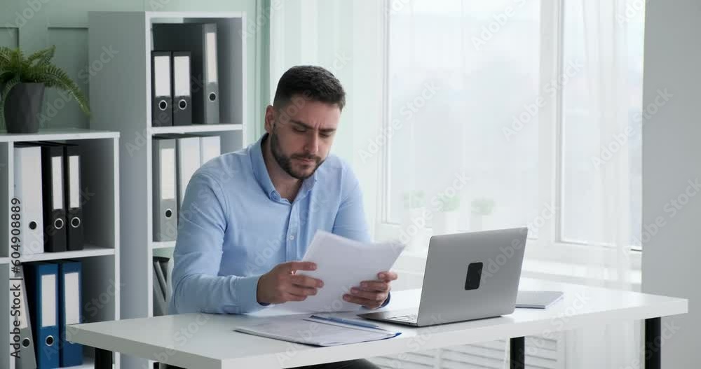 Busy businessman analyzing charts and graphs on documents at his desk. He checks data on his laptop and takes notes, trying to make informed decisions. Busy businessman analyzing charts and graphs on documents at his desk. He checks data on his laptop and takes notes, trying to make informed decisions.