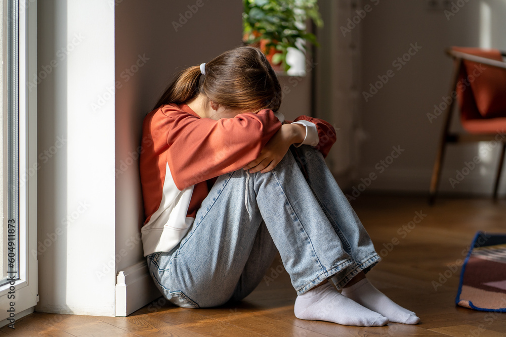 Depression in teens. Upset teenage girl sitting alone on floor and crying, feeling sad and depressed. Lonely teenager child having thoughts of suicide. Mental health of adolescents - obrazy, fototapety, plakaty 