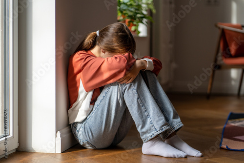 Depression in teens. Upset teenage girl sitting alone on floor and crying, feeling sad and depressed. Lonely teenager child having thoughts of suicide. Mental health of adolescents photo