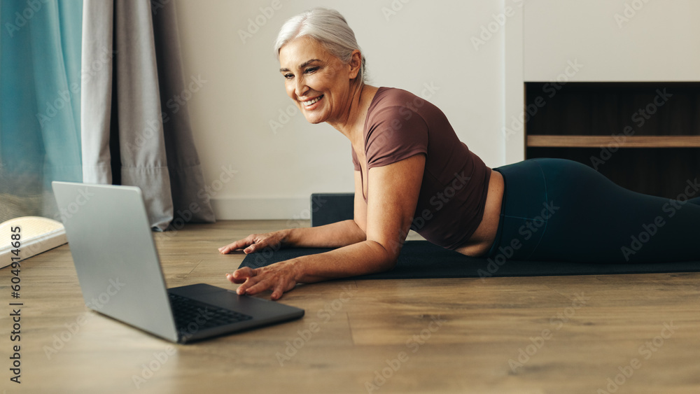 Happy senior woman browsing her laptop for online yoga classes at home Happy senior woman browsing her laptop for online yoga classes at home