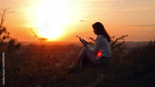 A long-haired girl reads a book in the sun. A young woman reads the Bible outdoors. A woman holds a Bible in her hands and studies the word of God on top of a mountain. Searching for truth