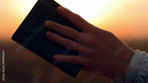 Close up Young Christian woman reading the bible, praying, putting her hand on the bible, sitting on a stone in nature, sunset in autumn evening, peace and tranquility, faith, God's blessing