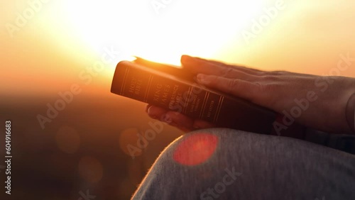 Close-up of a Bible in a woman's hands at sunset. Christianity