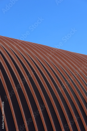 The roof of the hangar is made of stainless steel. The arched roof is made of metal construction. An industrial building in detail against a blue sky background. Construction. Vertical snapshot