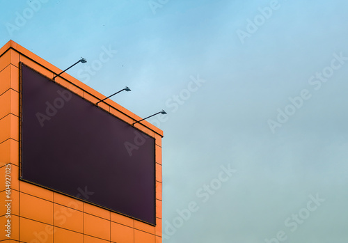 Empty black billboard with backlight on the wall of the building against the sky. Billboard mockup for advertising on the wall of the mall