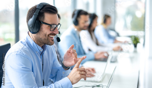 Professional customer support agent man counting on fingers while assisting customers at call center office, with colleagues in the background.