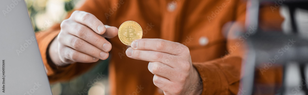 Fototapeta premium KYIV, UKRAINE - OCTOBER 18, 2022: selective focus of golden bitcoin in hands of successful businessman on blurred background in office, cropped view, banner