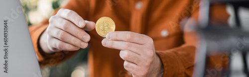 KYIV, UKRAINE - OCTOBER 18, 2022: selective focus of golden bitcoin in hands of successful businessman on blurred background in office, cropped view, banner