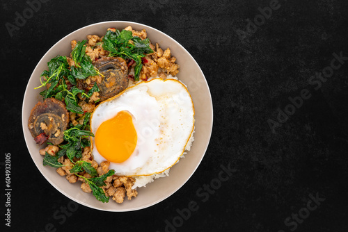 Khao Pad Ka Prao Kai Yeow Ma Kai Dao, Thai food, streamed rice with basil stir fried century egg, mince pork and fried egg in ceramic plate on dark tone texture background, top view