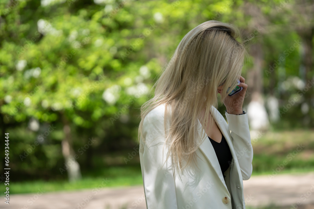 A young blonde woman in sunglasses stands on the street. The girl calls on a mobile phone.
