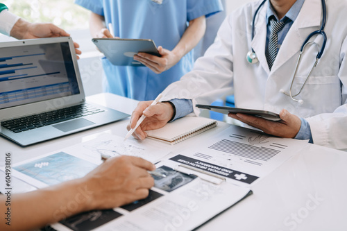 Medical team having a meeting with doctors in white lab coats and surgical scrubs seated at a table discussing a patients working online using computers in medical industry.