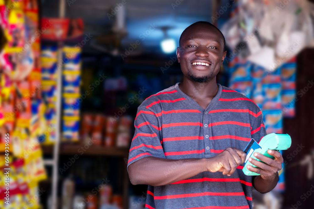 A black african man standing in front of a store holding a pos machine - obrazy, fototapety, plakaty 