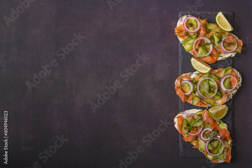 Open sandwiches with salted salmon, cream cheese, onions, capers, cucumber and microgreens on slate board with dark gray background. Seafood. Healthy food. Close up. Top view. Copy space 