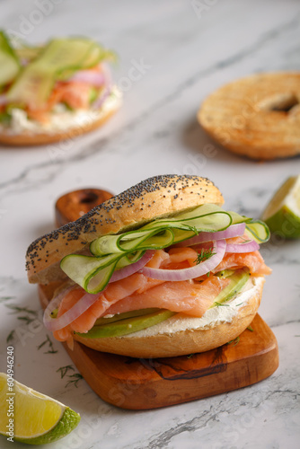 Salmon bagel sandwich with cream cheese, avocado, onions, cucumber on a wooden board. Close up. Copy space