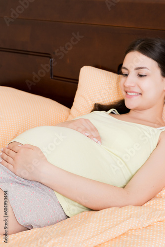 pregnant woman sitting in bed and touching her belly at home. pregnancy expectation concept
