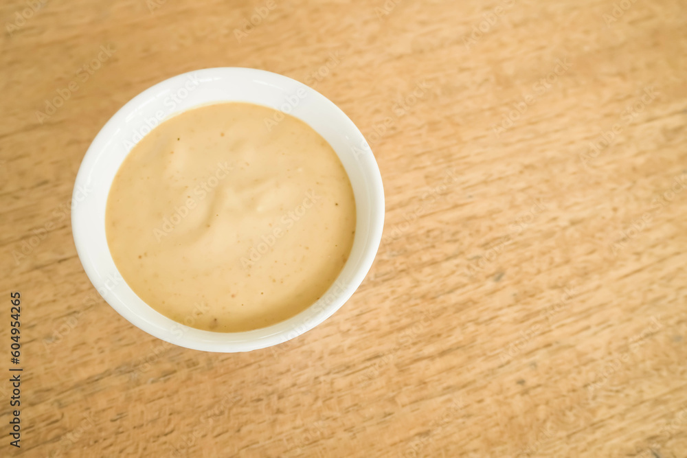 Roasted sesame dressing in the small white round bowl isolated on wooden background. Salad dressing, sauce, mayonnaise, oil. Copy text blank empty space - Top view photo. Roasted sesame dressing in the small white round bowl isolated on wooden background. Salad dressing, sauce, mayonnaise, oil. Copy text blank empty space - Top view photo.