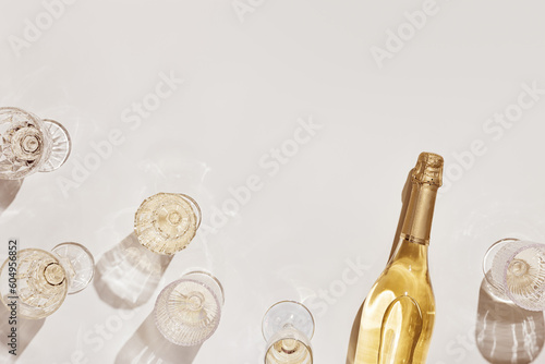 Flat lay with white sparkling wine bottle, set glasses wine with sunshine shadow and flare on light beige background. White wine aesthetic photo, copyspace. Summer holiday monochrome still life